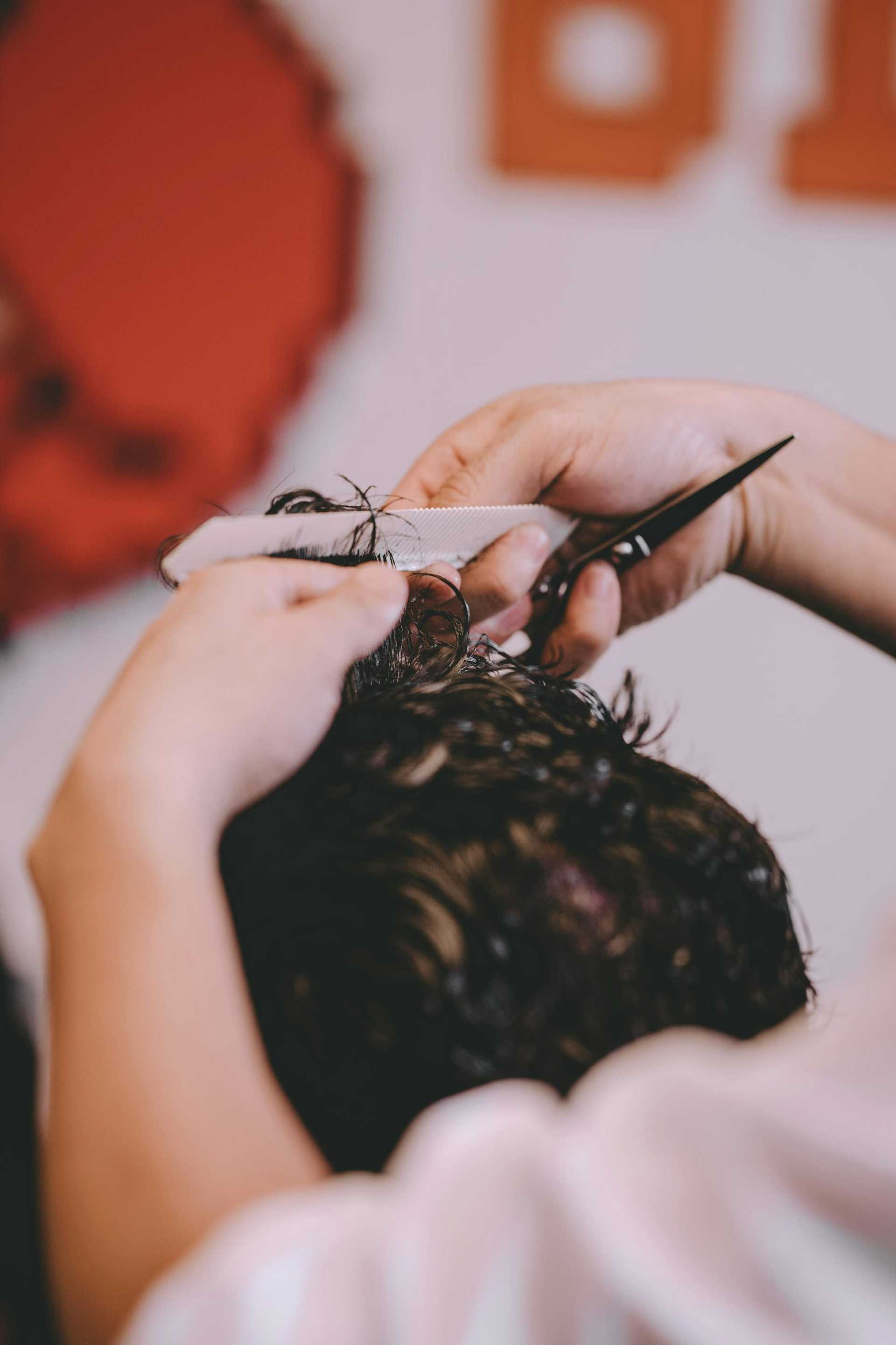 Hairdresser cutting hair with scissors and comb, close-up shot of the hands and tools in use.