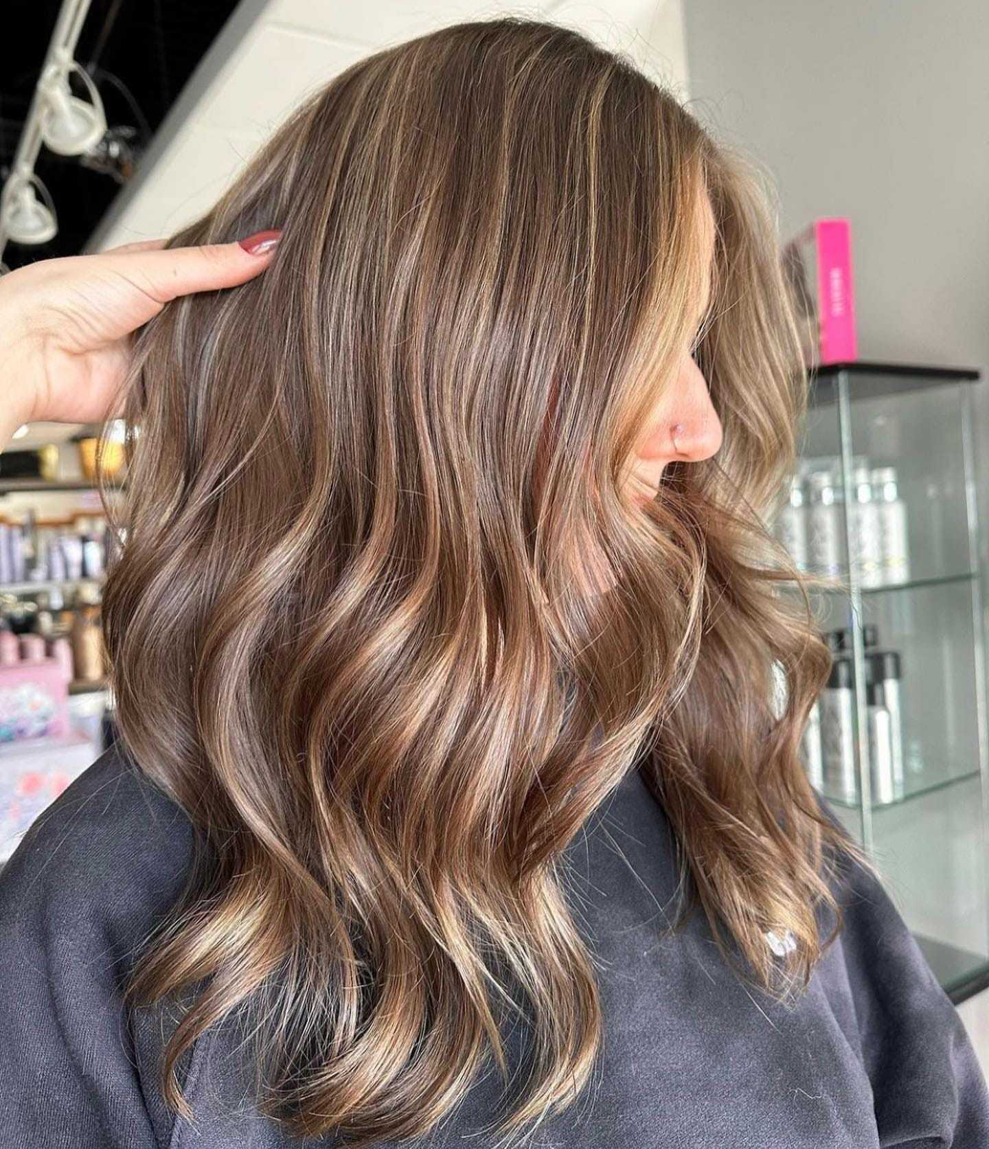 Woman with wavy, highlighted hair, viewed from the side, showcasing fresh salon hairstyle.