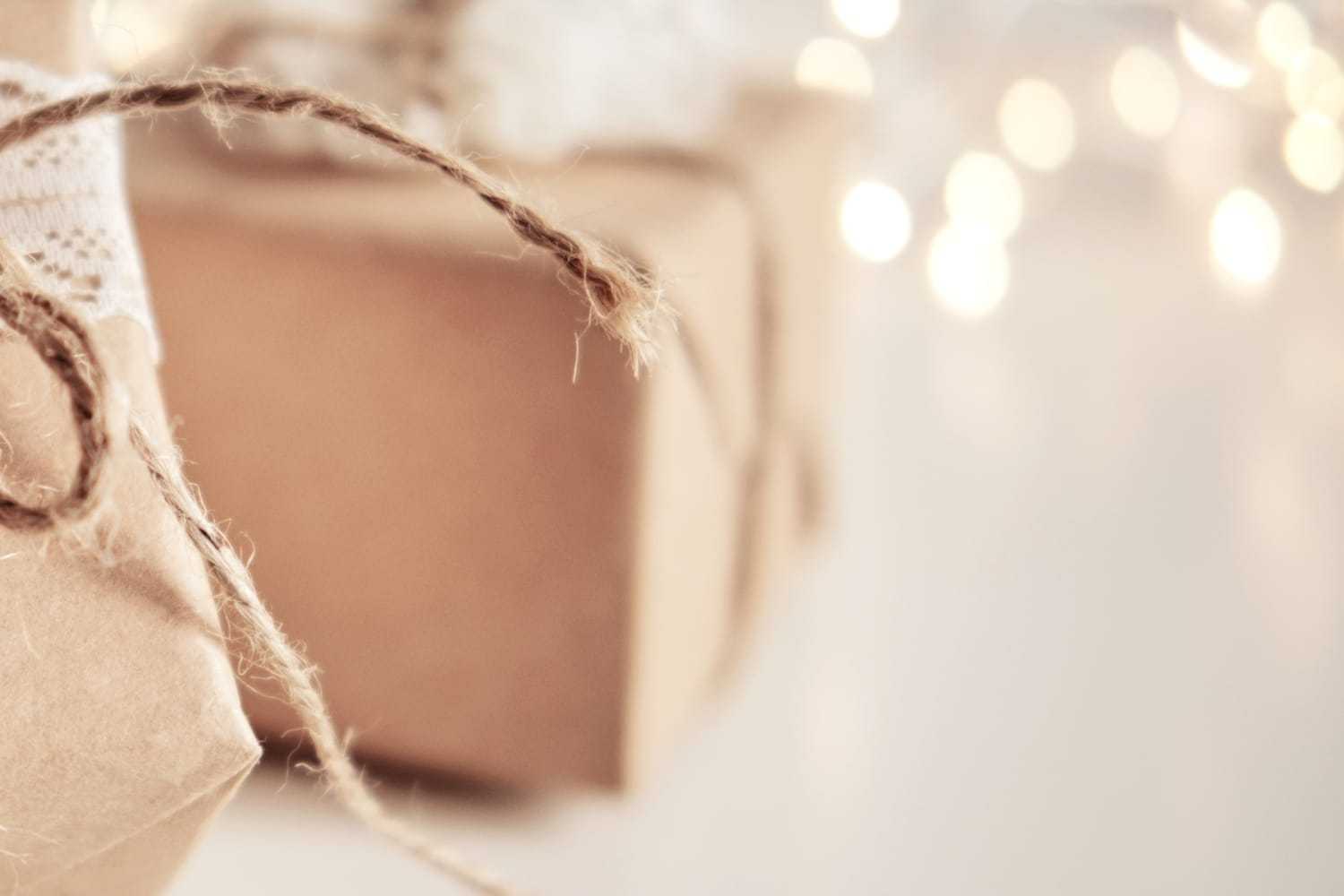 Brown paper gift wrapped with twine and lace against a blurred background of warm, white lights.